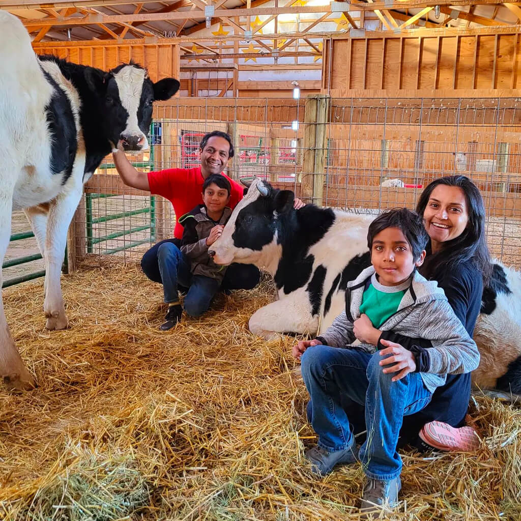 Founders, Shaleen and Shilpi Shahs standing next to a rescued cows and holding their children